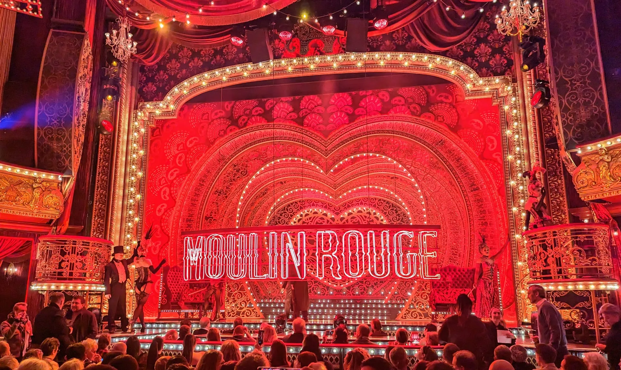 The Moulin Rouge set at the Piccadilly Theatre, a vast red and gold proscenium with the neon Moulin Rouge sign lit above the stage