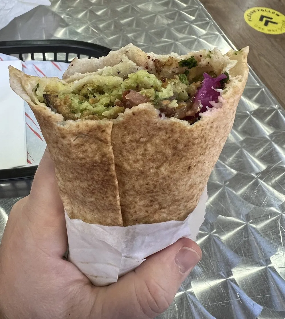A falafel wrap in flatbread held in one hand, filled with salad, pickles and red cabbage