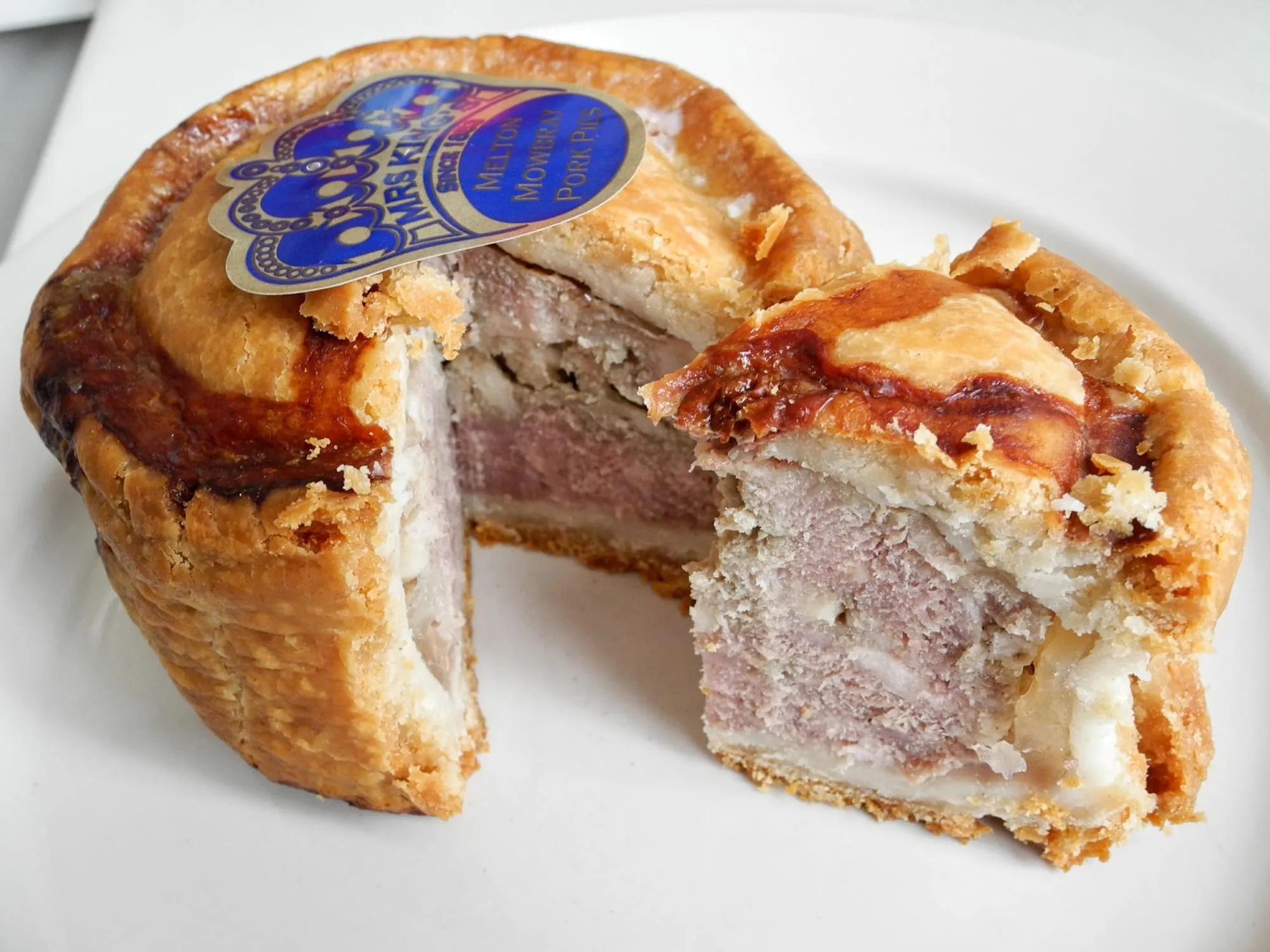 A pork pie sliced in half, showing the pastry shell, pink pork filling and a pale layer of jelly between the meat and the crust.