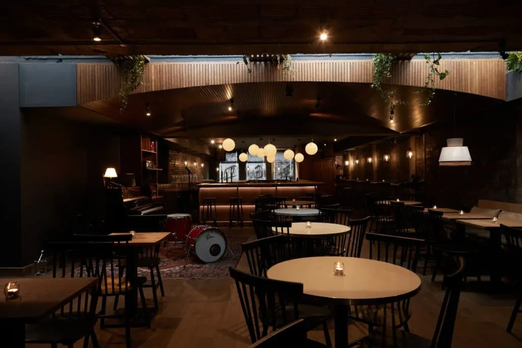 Mu's dining room, with round tables in front of a small stage holding a piano and a drum kit