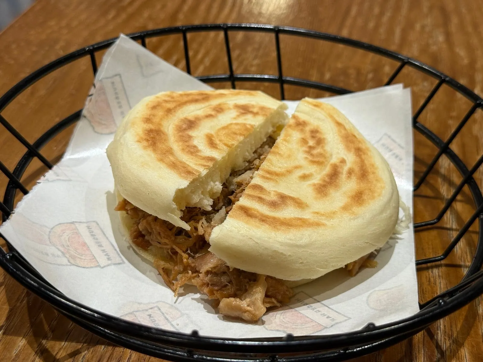 A rou jia mo flatbread bun split open to show shredded, spiced meat filling, in a wire basket