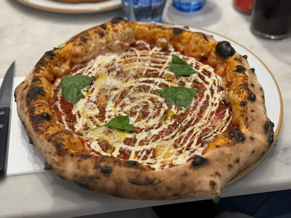 A Neapolitan pizza at Napoli on the Road with a puffed, leopard-spotted crust, tomato and mozzarella swirled across the base and fresh basil leaves on top