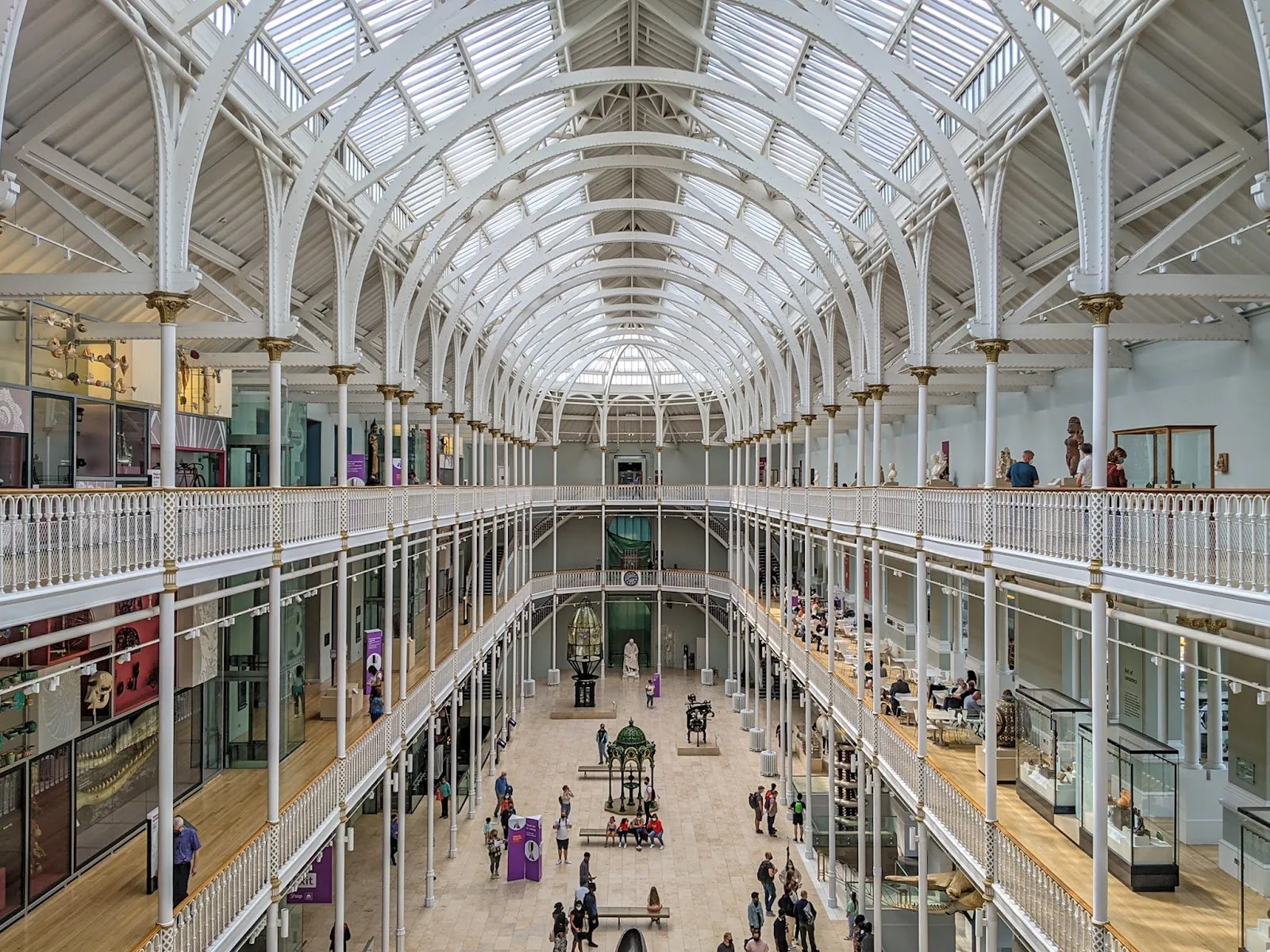 The National Museum of Scotland's Grand Gallery, a long hall of white cast-iron columns and arches under a glazed roof, seen from an upper balcony