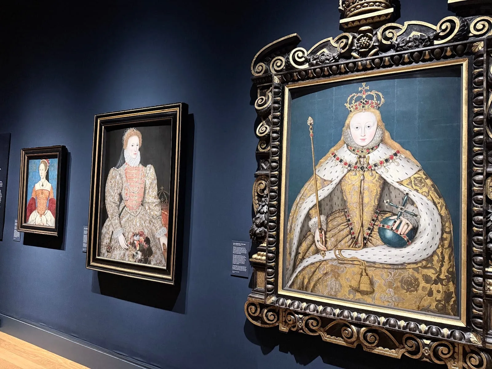 Tudor-era portraits on a dark blue wall, including a crowned queen in gold robes holding a sceptre and orb