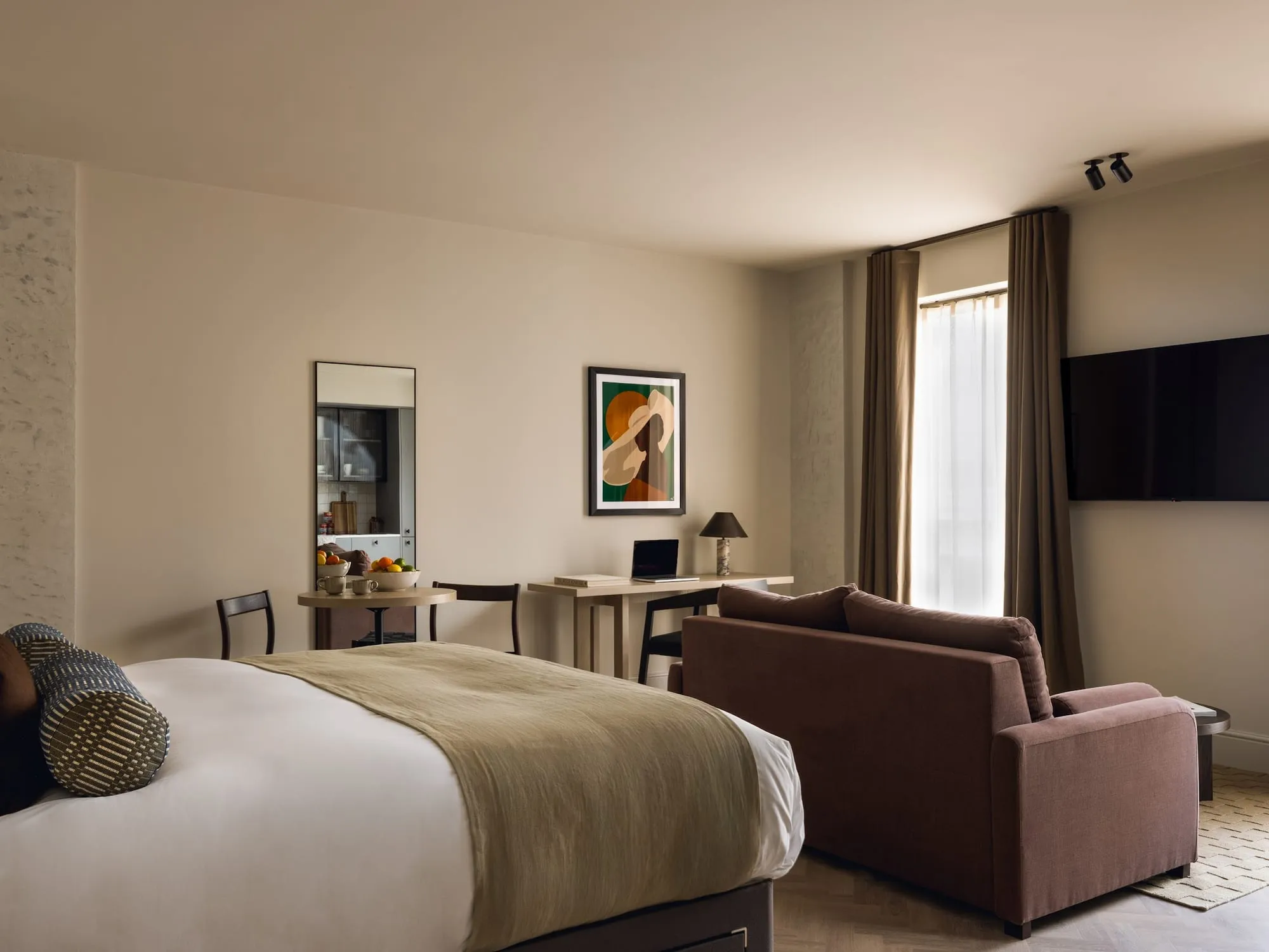 A studio at Native Fulham, with the bed in the foreground, a round table for two and a sofa beside the window
