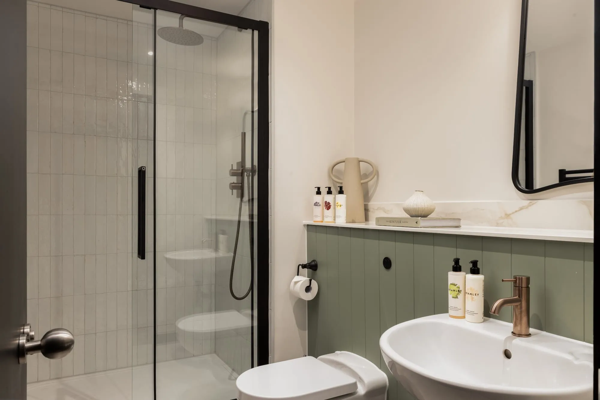 The bathroom at Native King's Wardrobe, with white tile, a glass shower enclosure and sage-green wall panelling