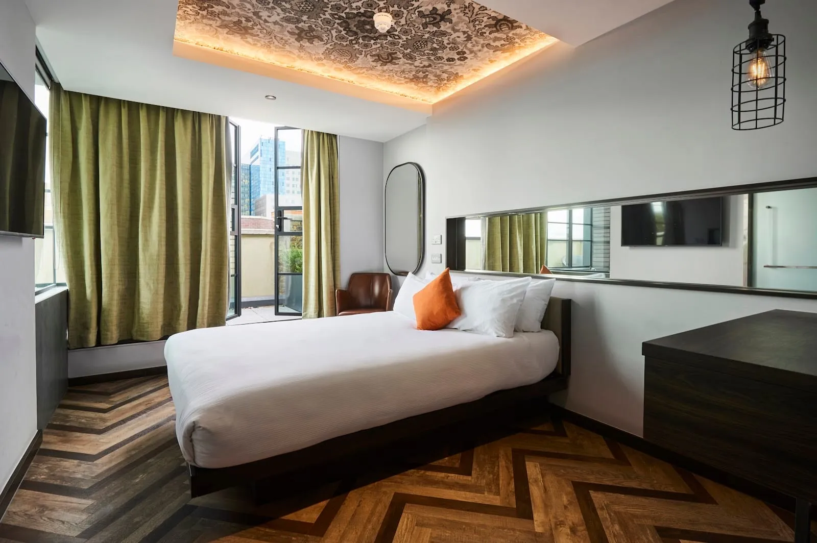 A double room at New Road Hotel with green curtains, a herringbone wooden floor and a tall window