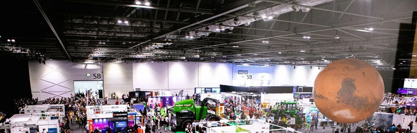A packed exhibition hall at New Scientist Live, exhibitor stands beneath a giant model of Mars suspended from the ceiling