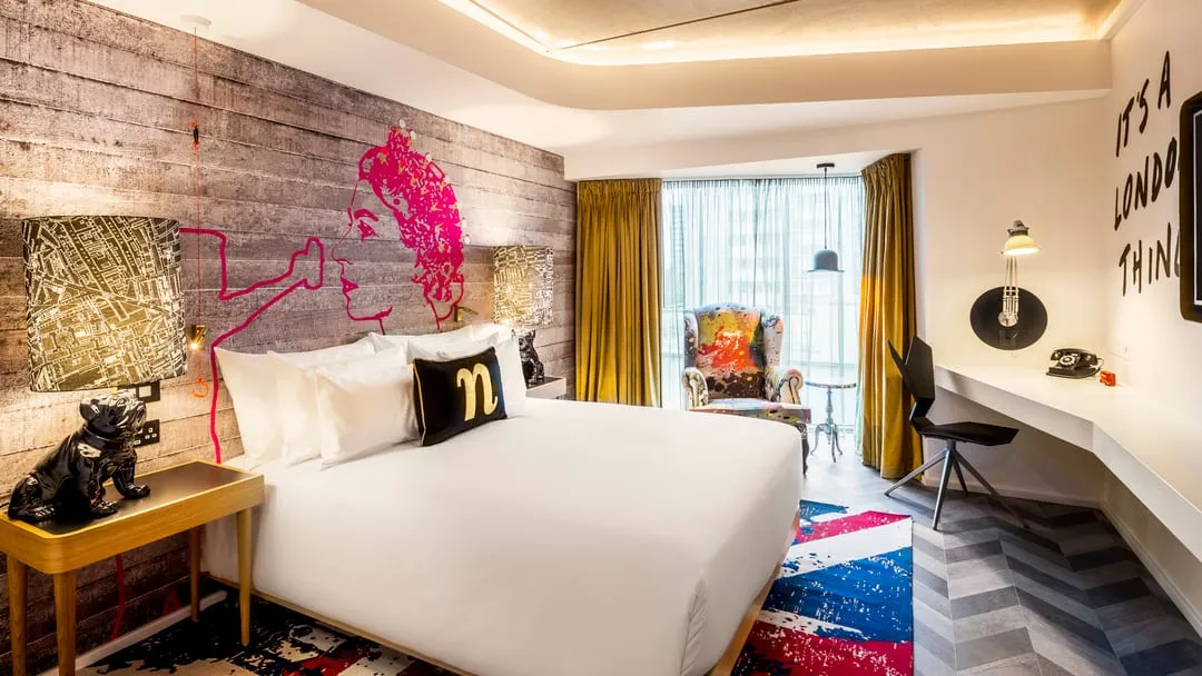 An nhow London room with a pink pop-art portrait of the Queen on a wood-panelled wall, the words "IT'S A LONDON THING" painted beside it, and a Union Jack-patterned rug
