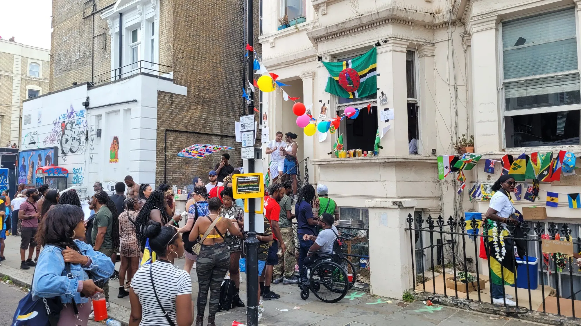A decorated Georgian townhouse hung with Caribbean flags and balloons on the Notting Hill Carnival route, with a crowd gathered outside
