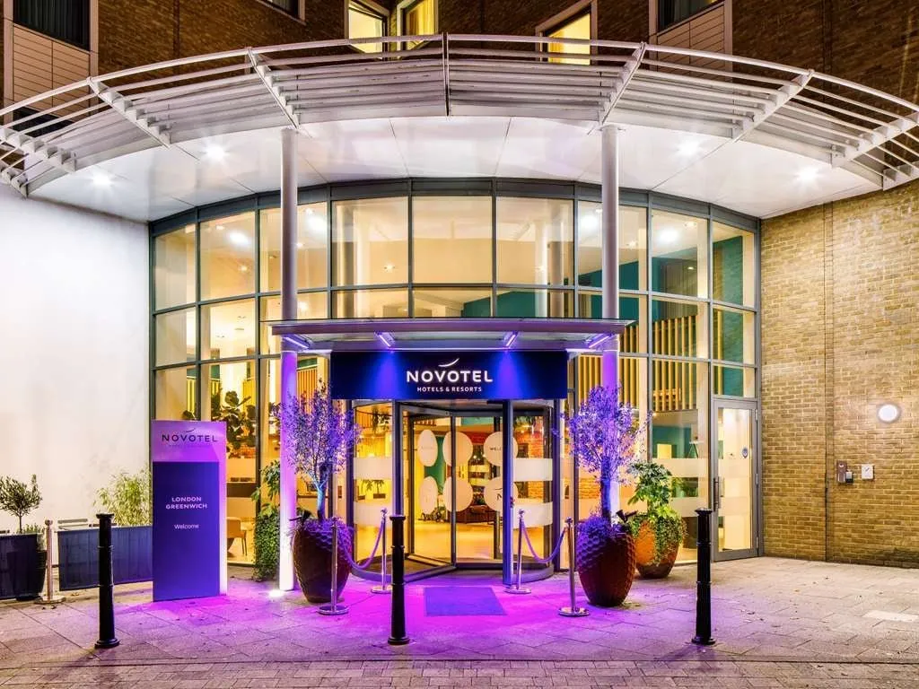 The revolving-door entrance of Novotel London Greenwich, lit at dusk