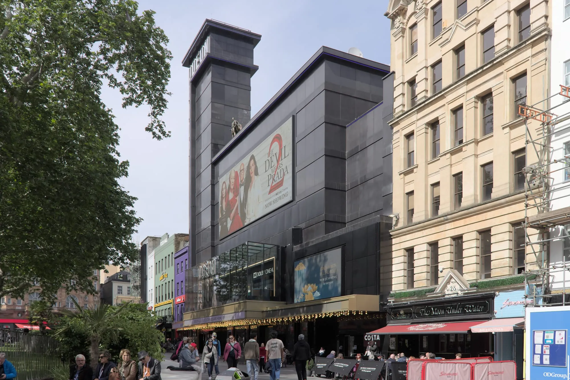 The black-clad tower and front of Odeon Luxe Leicester Square, seen from the garden in the middle of the square