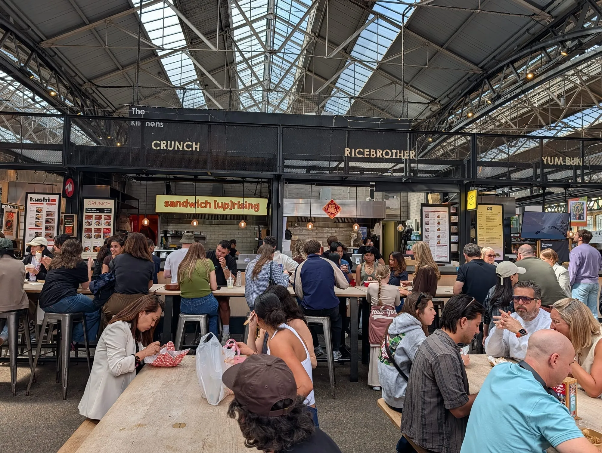 Long communal tables full of people eating in front of the food counters at Old Spitalfields Market