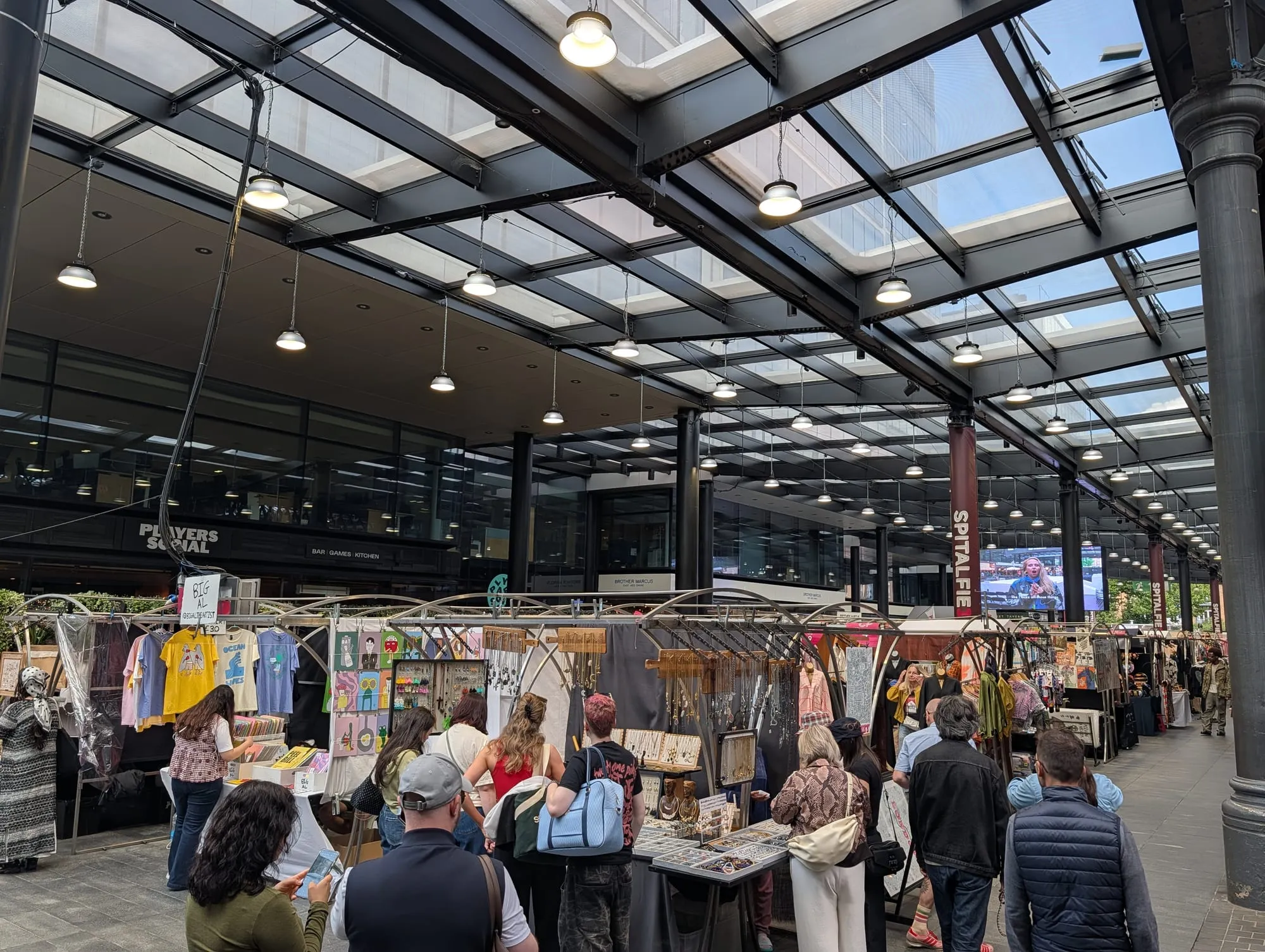 Traders' stalls under the glass and iron roof of Old Spitalfields Market, busy with shoppers