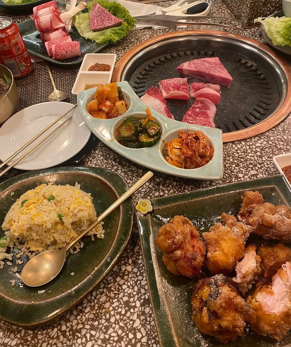 Heavily marbled raw beef laid out on a domed grill at Olle, with a boat-shaped tray of kimchi and pickled cucumber, a plate of egg fried rice and a plate of fried chicken