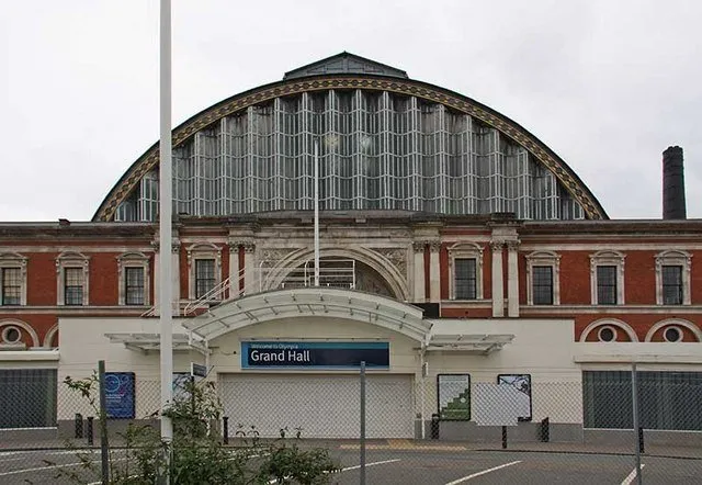 The exterior of Olympia London's Grand Hall, its arched glass roof above a Victorian brick facade and an entrance sign reading Grand Hall