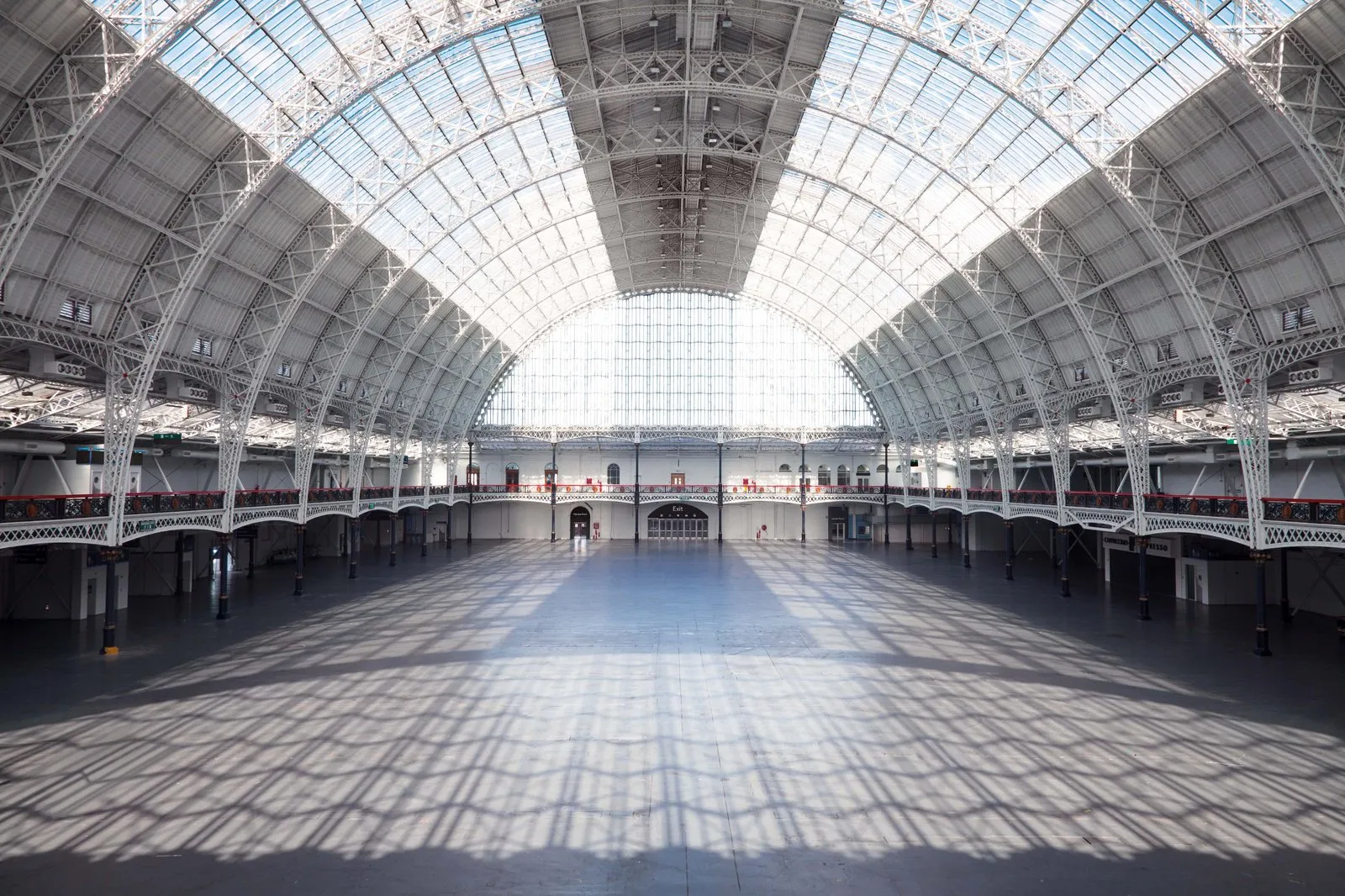The barrel-vaulted glass roof and cast-iron arches of Olympia London's Grand Hall, empty and lit by daylight