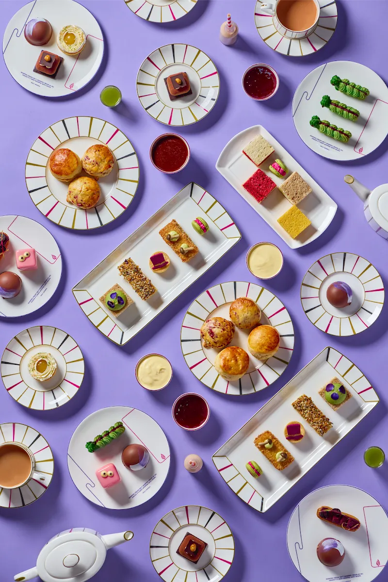 An overhead view of the Charlie and the Chocolate Factory afternoon tea at One Aldwych, laid out on lilac with striped plates, caterpillar cakes, coloured sponge squares and scones