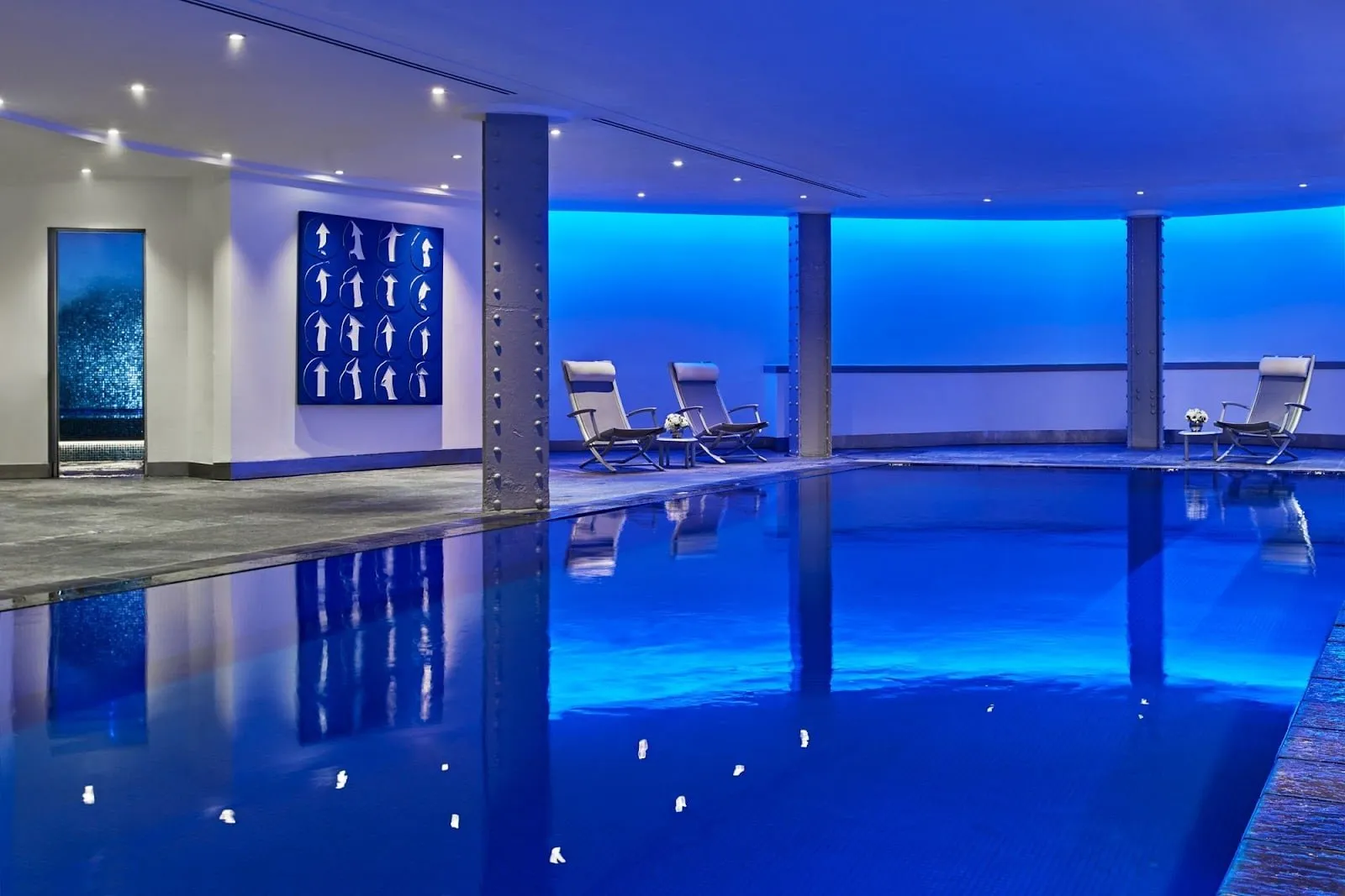 The underground pool at One Aldwych, lit blue, with loungers along the far side