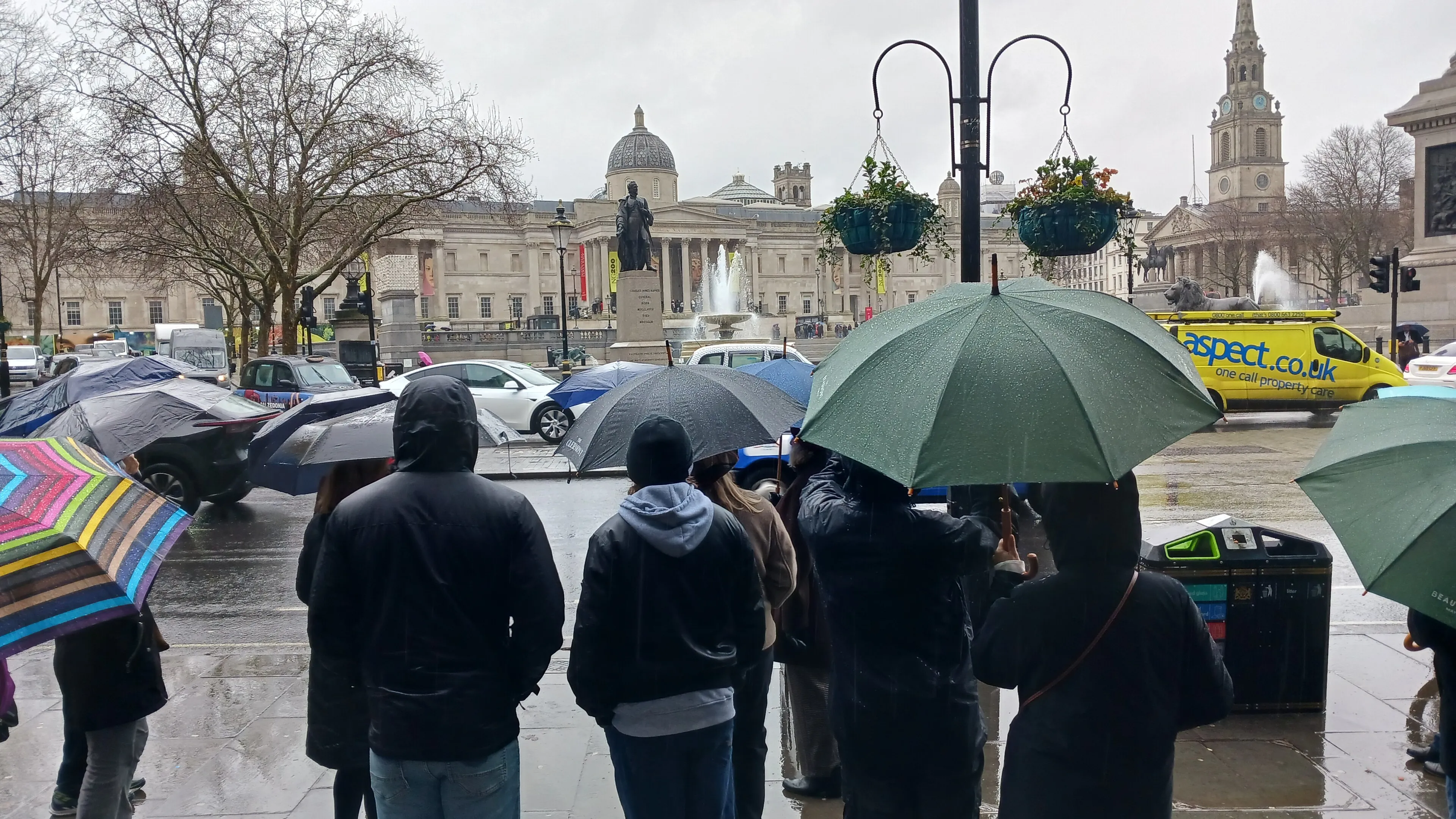 Visitors carrying umbrellas through Trafalgar Square on a rainy day