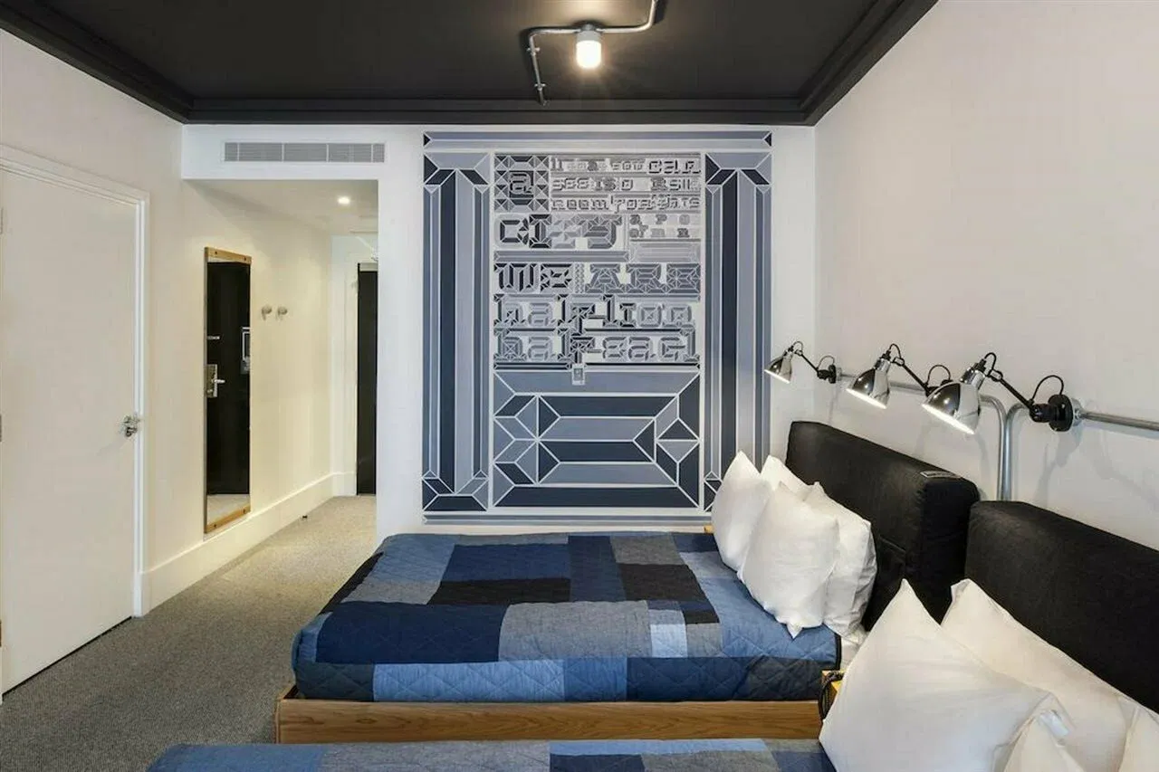 A twin room with a large grey geometric mural above the beds, patchwork denim quilts, a black ceiling and adjustable wall lights