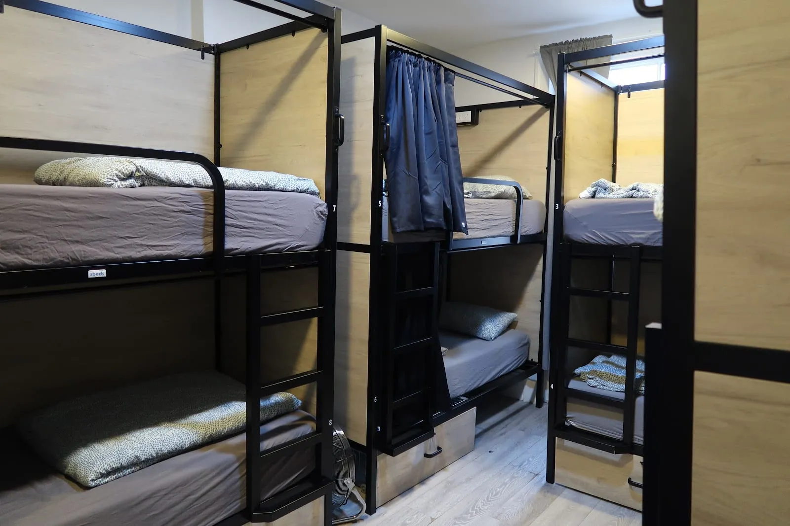 One of the curtained pod-style bunks at Onefam Notting Hill, each bed numbered and fitted with its own curtain
