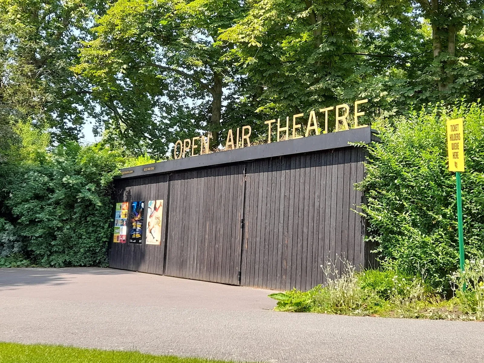 The wooden entrance gate to the Open Air Theatre, with the venue's name in gold letters above and a ticket holders' queue sign beside it