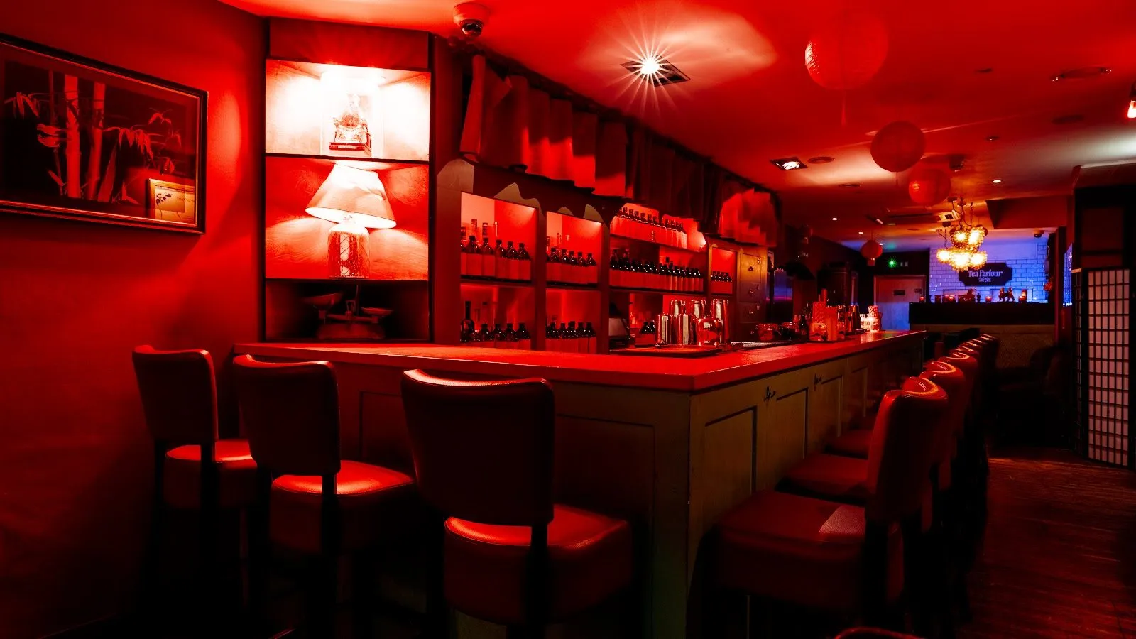 One of Opium's bars, lit red, with leather bar stools, shelves of bottles, paper lanterns and a lamp in a wall niche