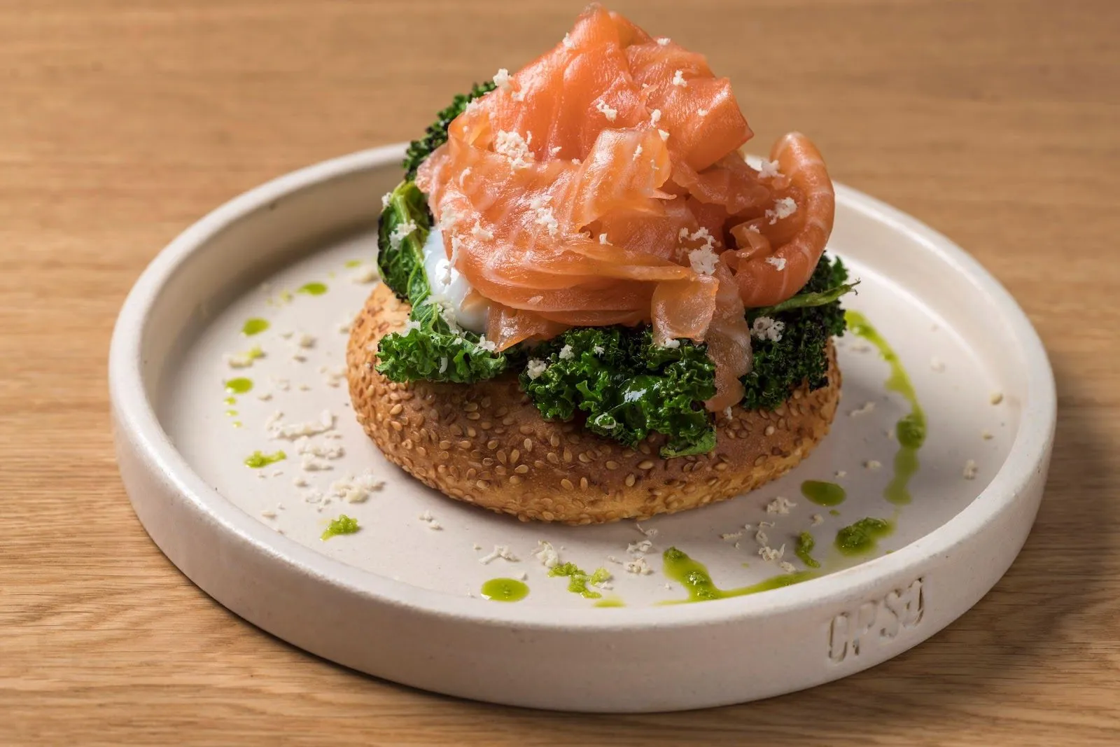 Smoked salmon and kale on a sesame bun, on a pale plate stamped OPSO