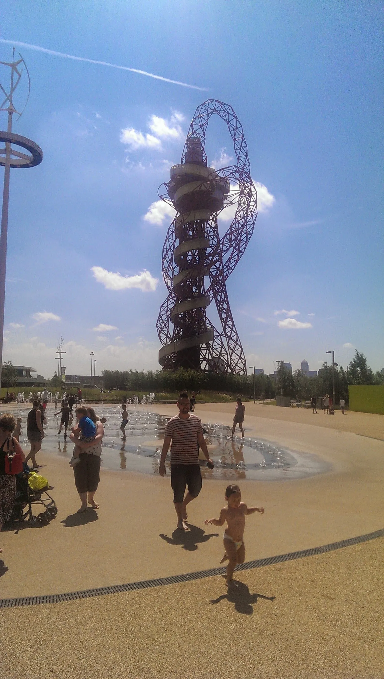 The ArcelorMittal Orbit rising above the fountains in Queen Elizabeth Olympic Park, with children playing in the water