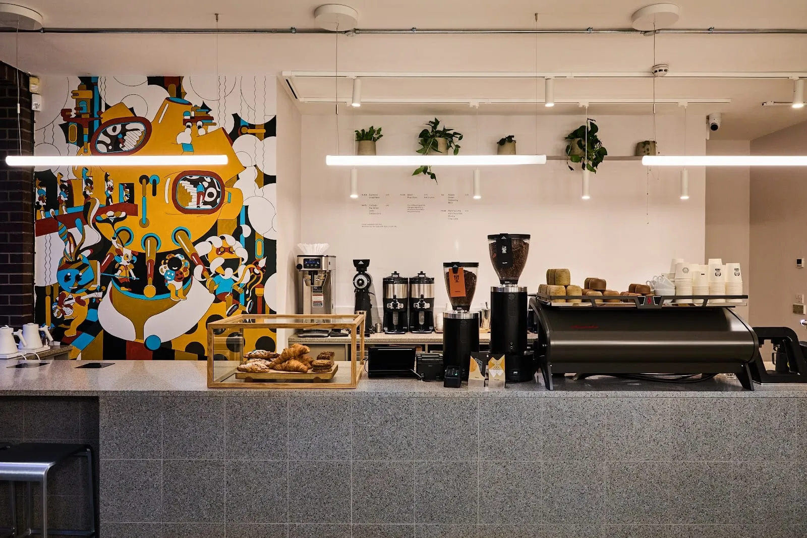 The counter at Origin Coffee Roasters, with a large colourful mural on the wall and pastries in a glass case