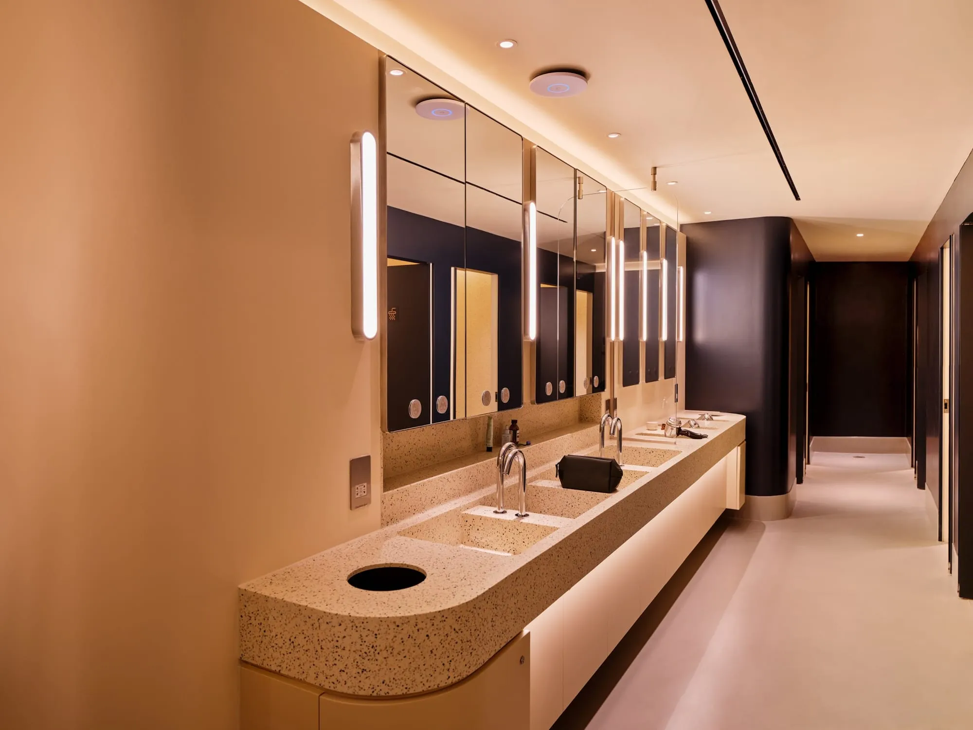 The shared bathroom at Otherwander Soho, with a long vanity counter holding several inset sinks and a corridor of stalls beyond