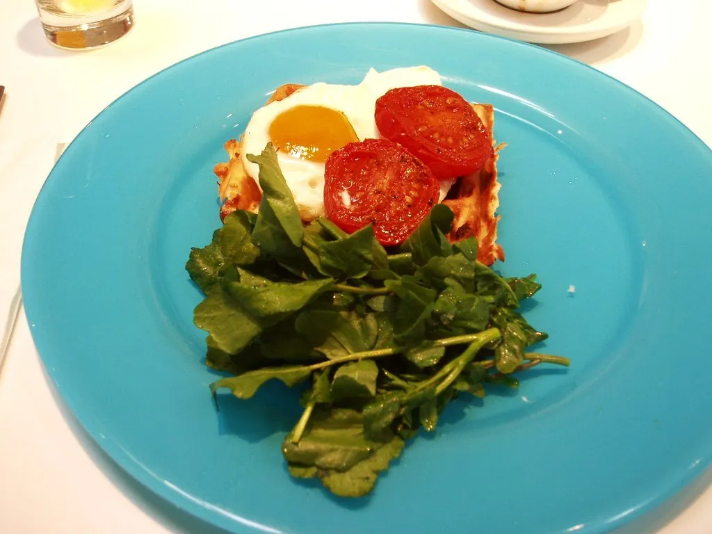 A slice of tart with poached egg, tomato and watercress on a blue plate