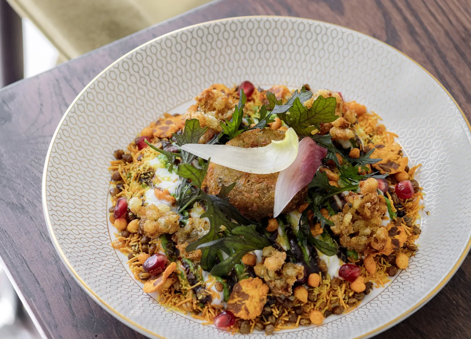 A composed Awadhi dish at Oudh 1722 with spiced patty, yoghurt, sev, pomegranate seeds and greens in a gold-patterned bowl