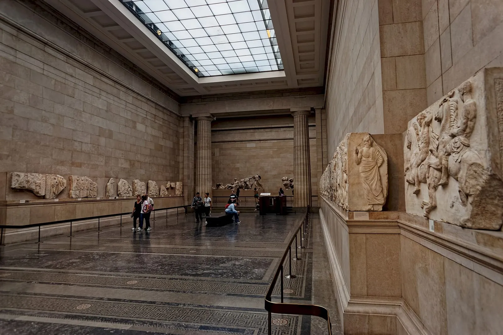 The Duveen Gallery, a long stone hall with a skylight, Parthenon frieze panels along the walls and pediment sculptures at the far end