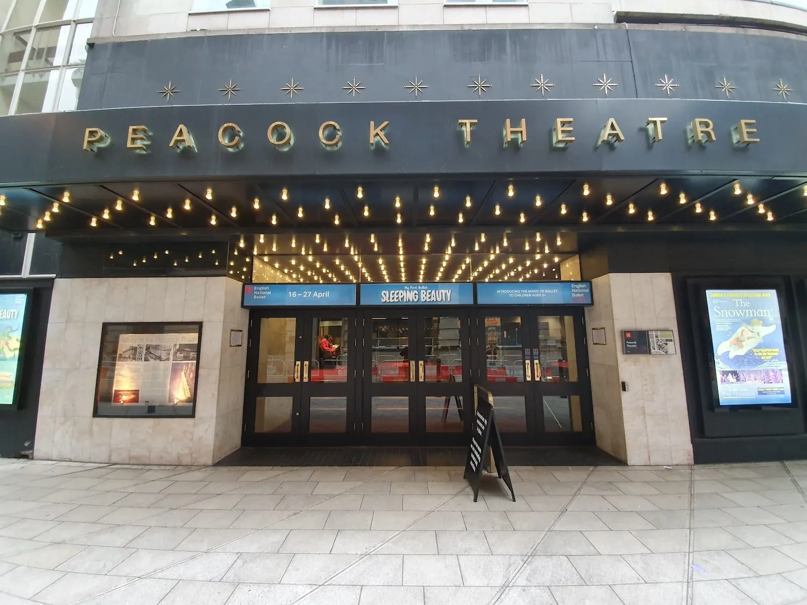 The Peacock Theatre's entrance, with its name in gold letters above a canopy of bare bulbs and glass doors beneath
