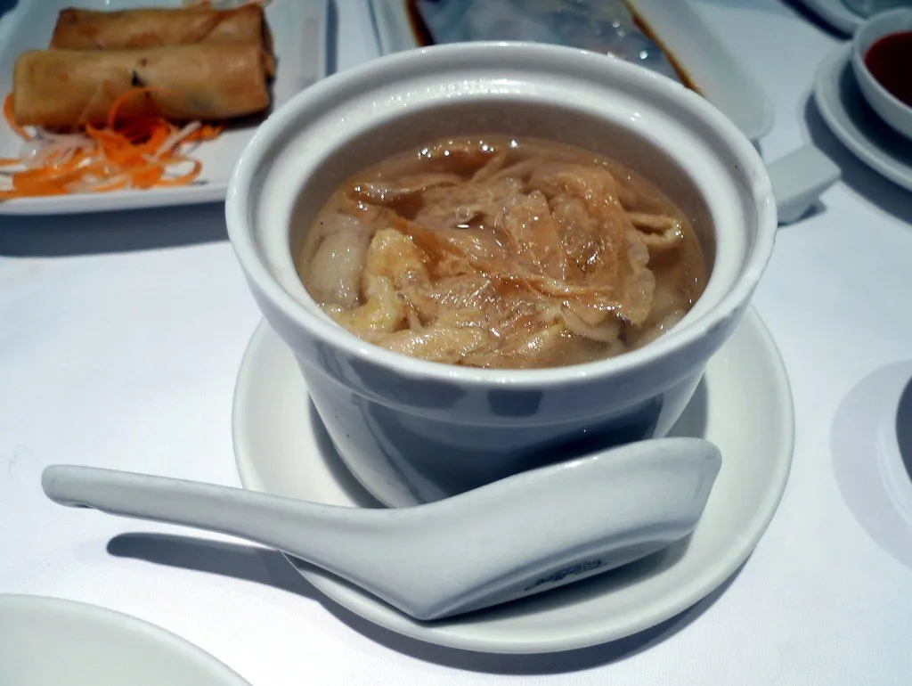 A steamed rice noodle roll in soy sauce on a white plate