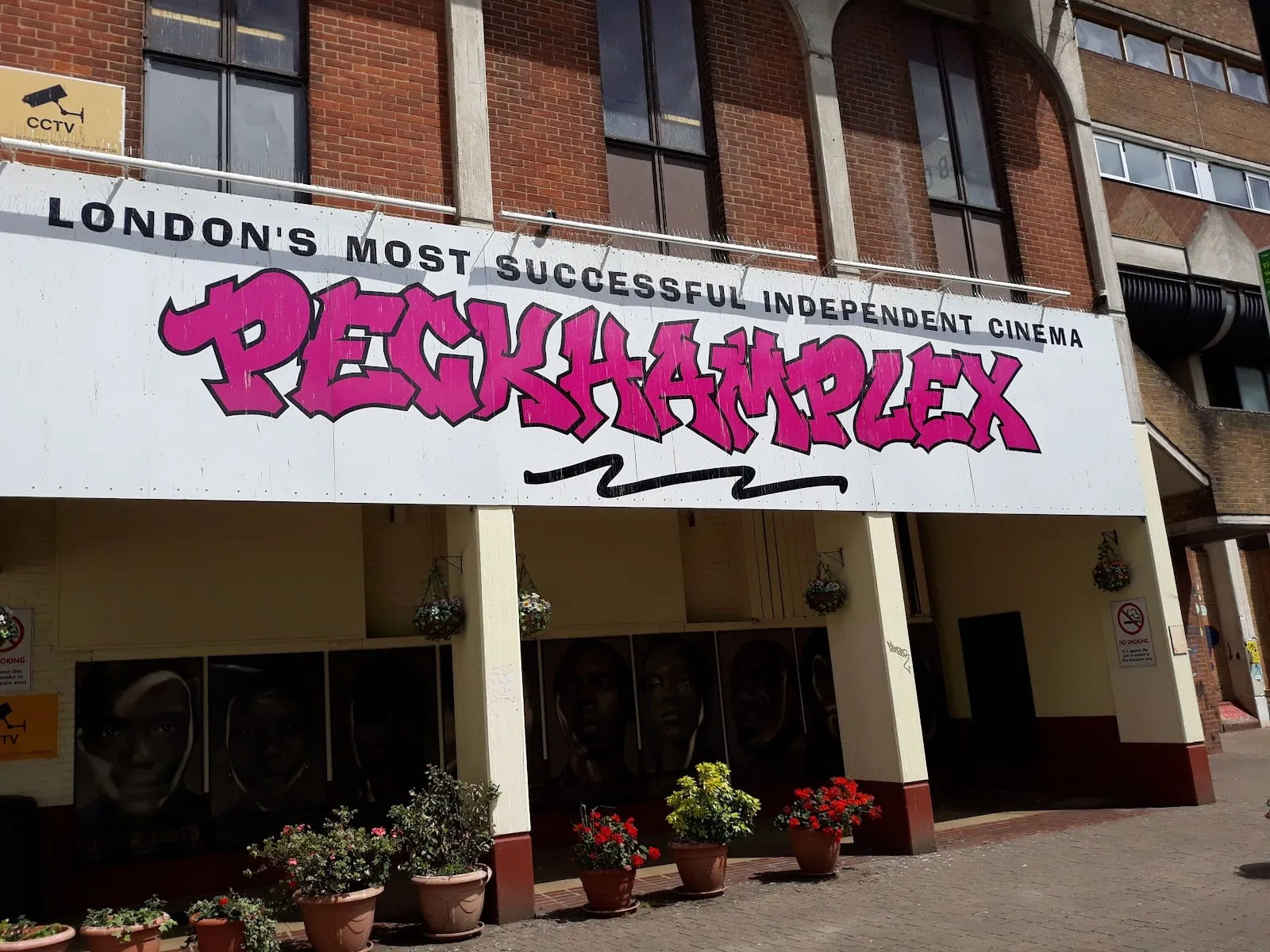 The pink PECKHAMPLEX sign above the cinema's brick frontage, with potted plants either side of the entrance