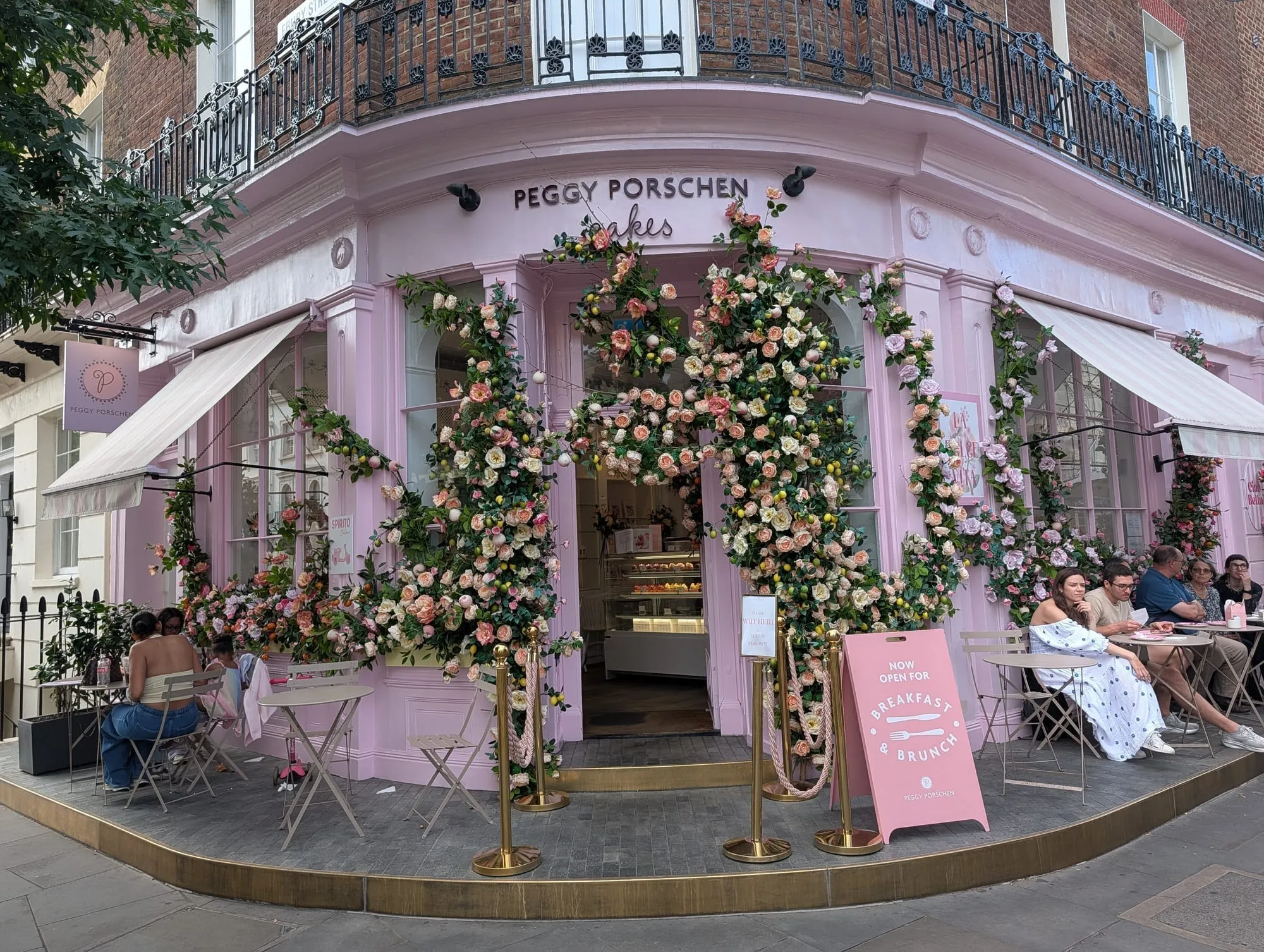 The pink Peggy Porschen shopfront on a corner, its windows and doorway framed by dense floral displays
