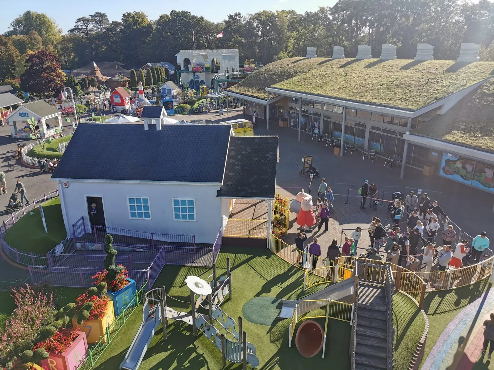 Peppa Pig World at Paultons Park from above: Peppa's schoolhouse, a crowd queueing to meet Peppa on the veranda, and a playground in the foreground