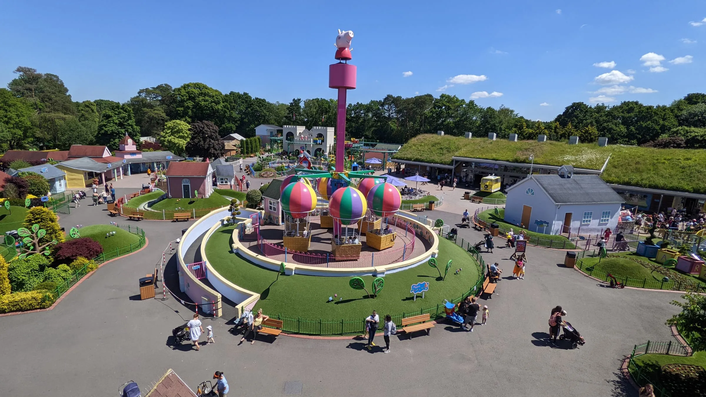 Peppa Pig World at Paultons Park from above, Peppa's Big Balloon Ride turning in the centre with its striped balloons and a Peppa figure on top, families walking the paths around it