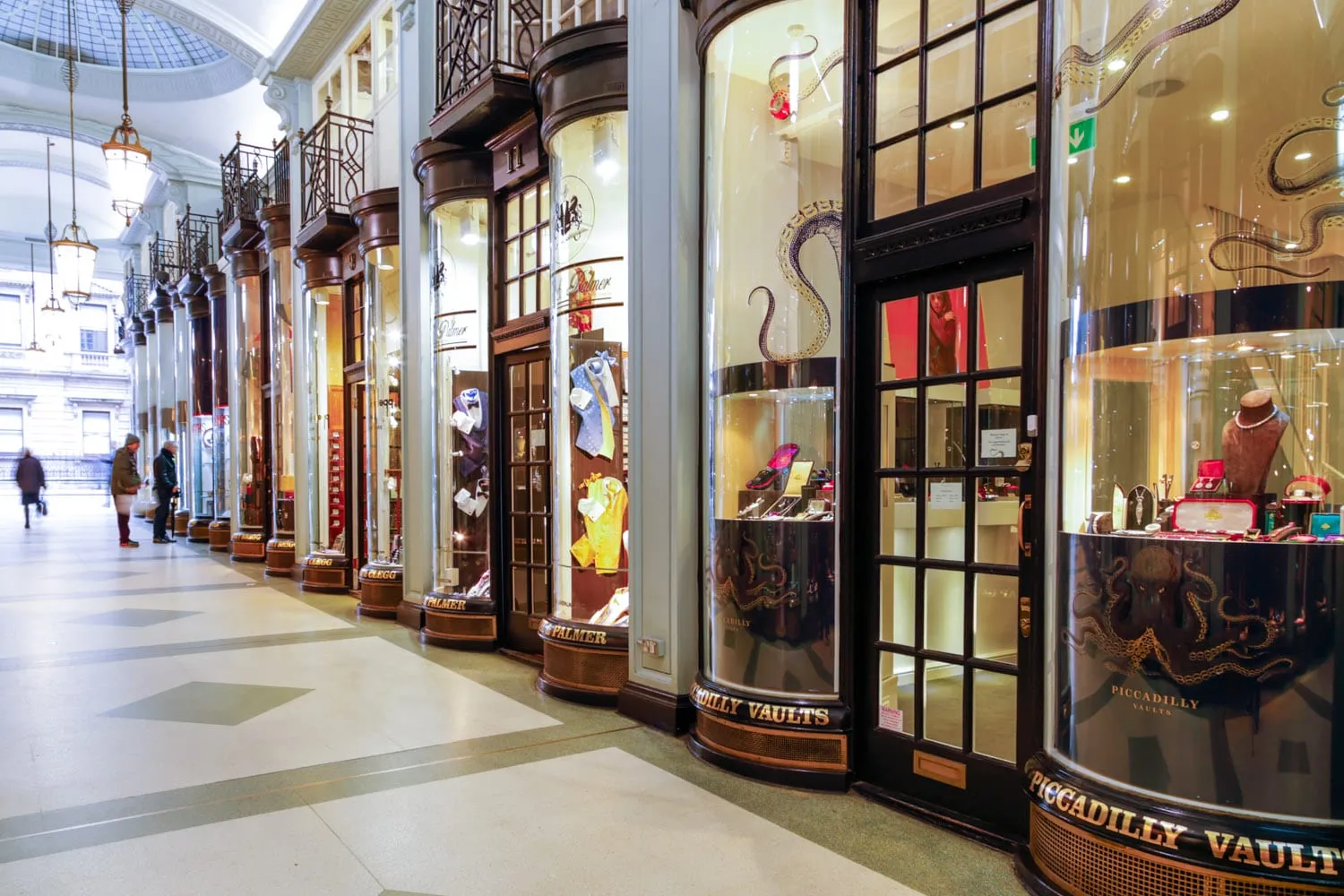 The glass-domed interior of Piccadilly Arcade lined with shopfronts, including the Piccadilly Vaults jewellers