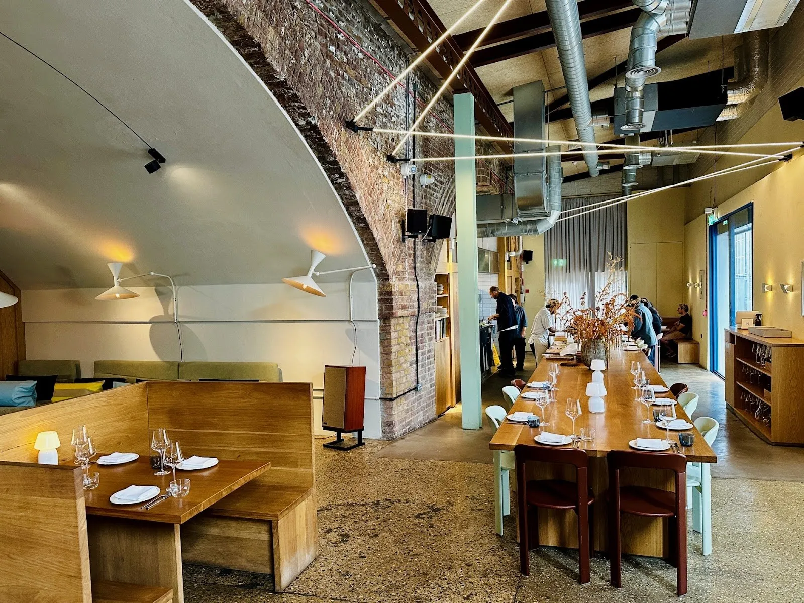 A long communal table and booths under an exposed brick railway arch