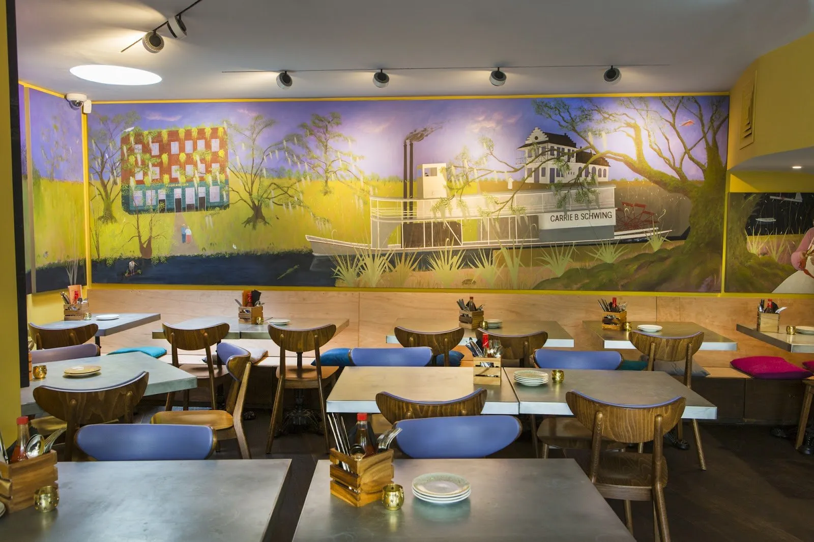 Tables beneath a painted mural of a Louisiana paddle steamer and the Plaquemine Lock building