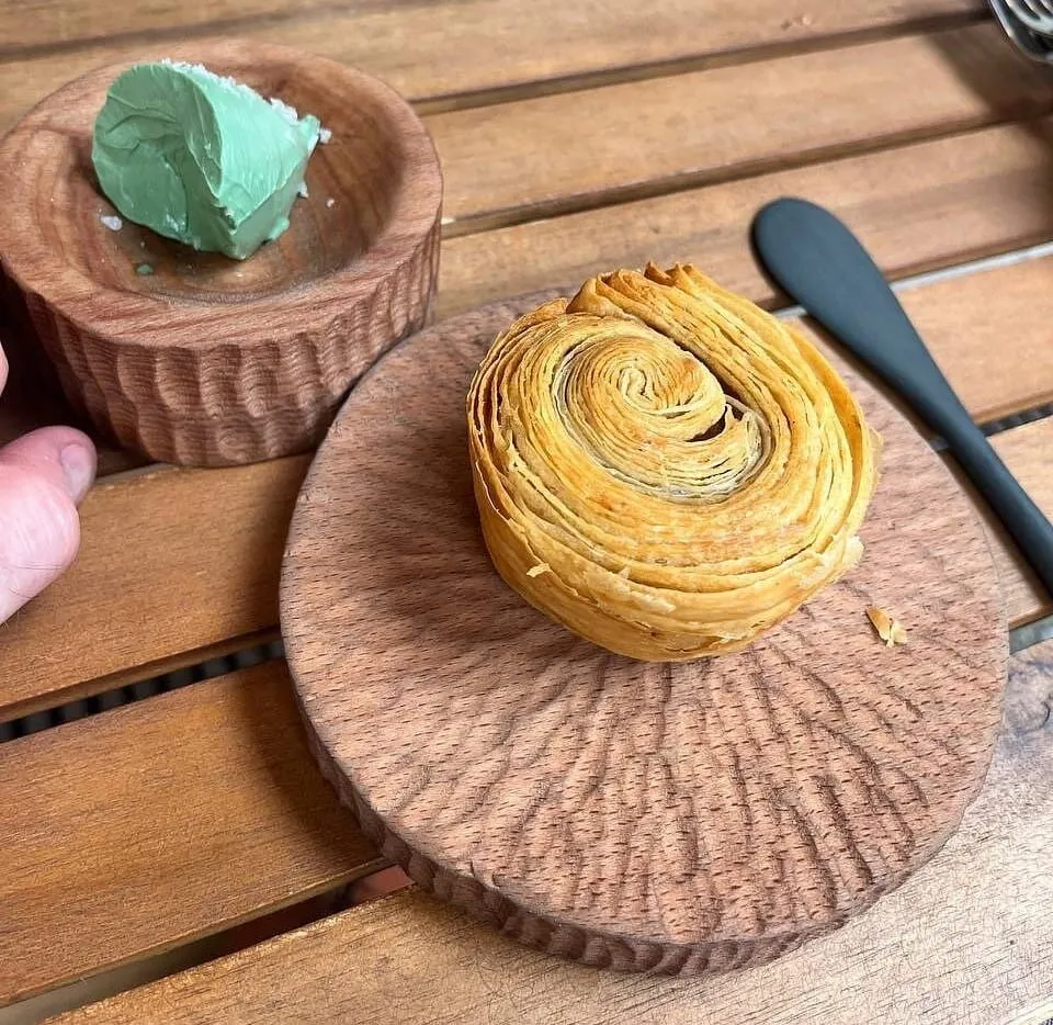 A laminated pastry spiral served on a small wooden board at Plates, with a quenelle of green butter in a wooden pot alongside