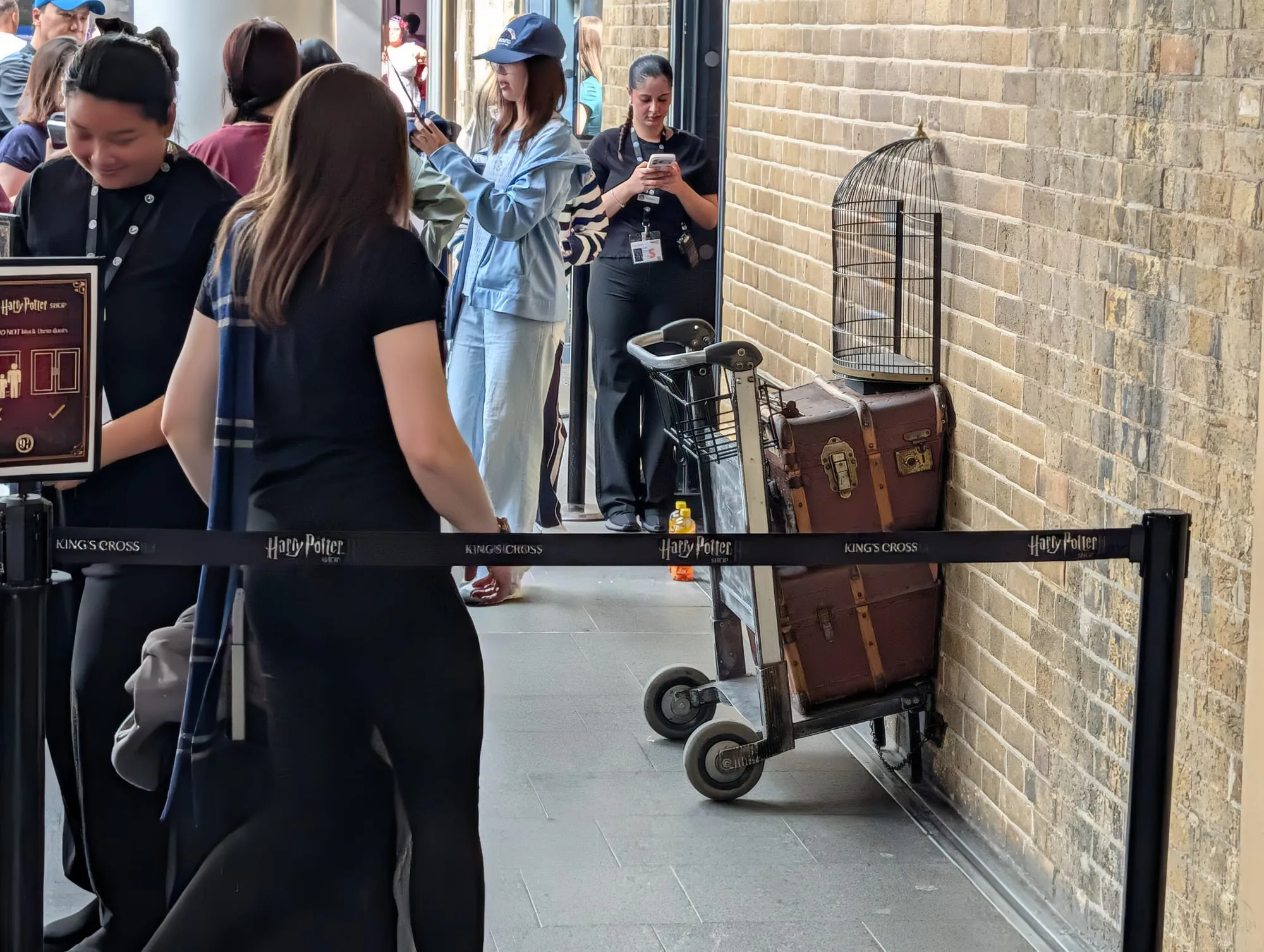 A luggage trolley half-embedded in the wall at Platform 9 3/4, with an owl cage on top