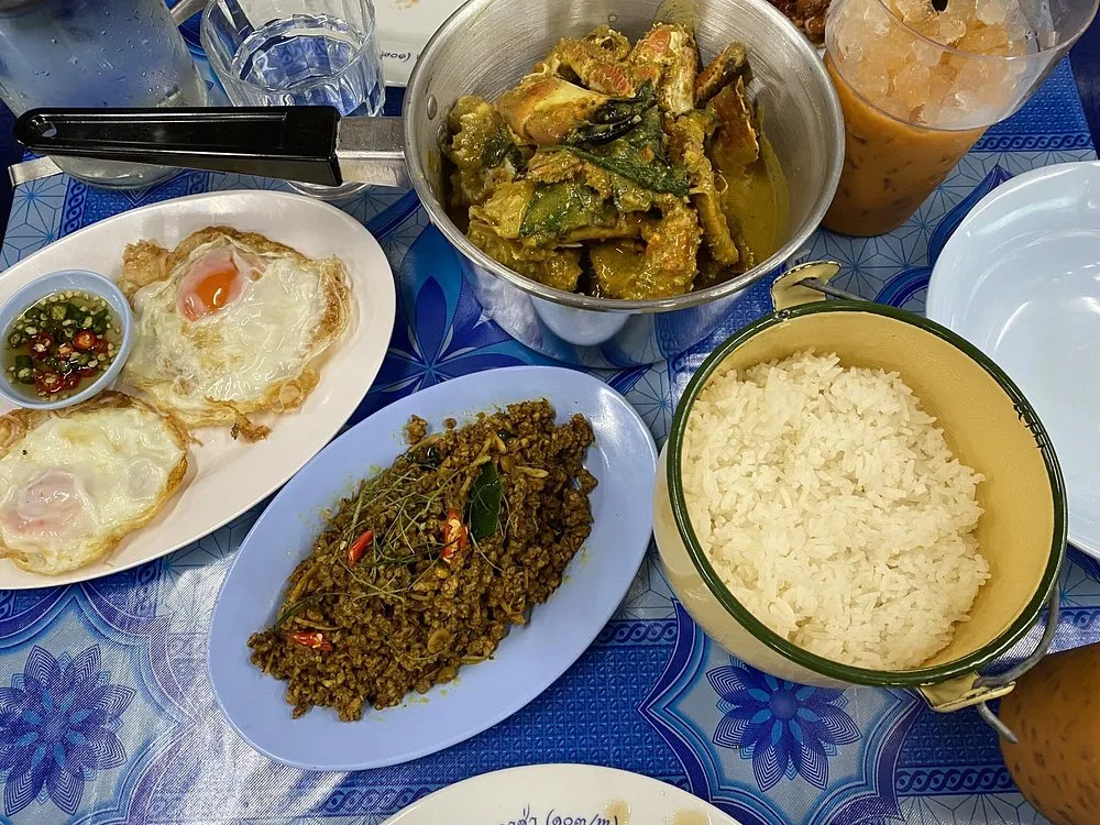 A shared spread of fried eggs, a minced meat stir-fry, a pot of yellow curry, jasmine rice and iced tea on a blue floral cloth