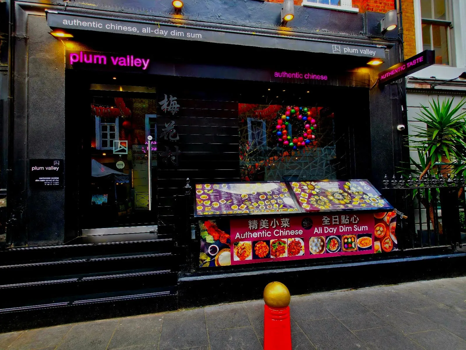 Plum Valley's black shopfront on Gerrard Street, with pink neon signage, a wreath and a dim sum menu board outside