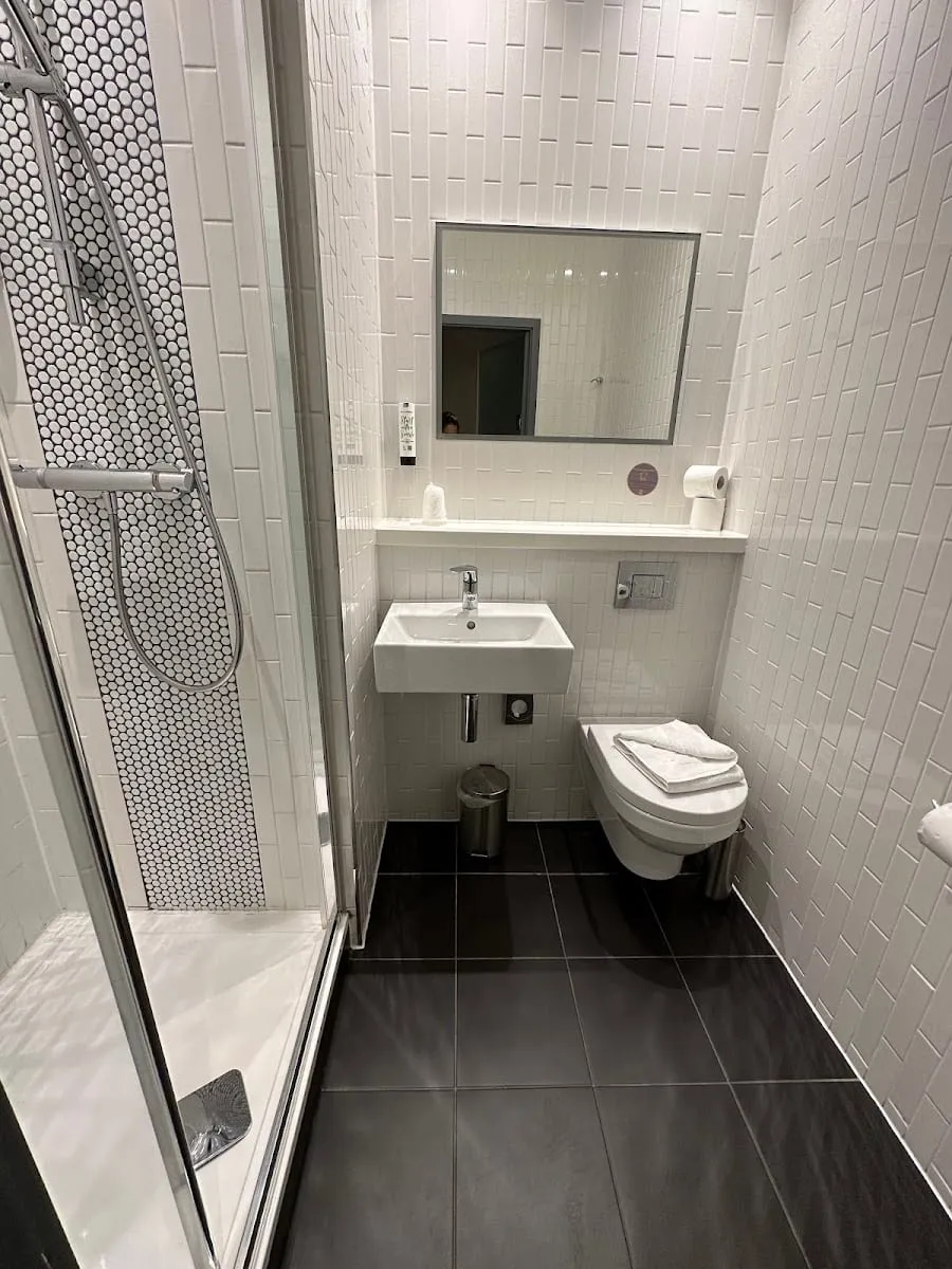 The ensuite bathroom of a Point A Kensington room, with white subway tile, a penny-round tiled shower and dark floor tiles
