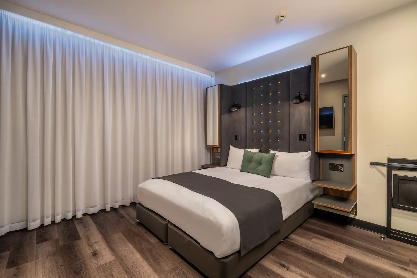 A room at Point A Kensington with a floor-to-ceiling curtain, a dotted headboard panel and a wall-mounted mirror and TV